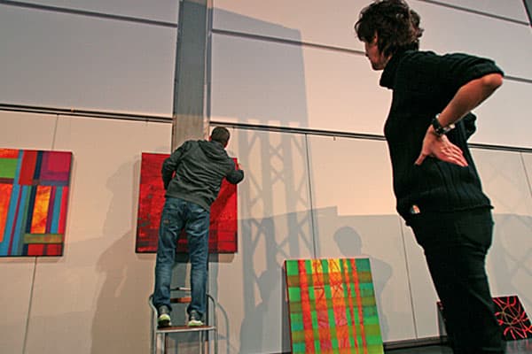 Aufbau der Ausstellung: eine Person hängt ein Gemälde auf einer Leiter auf