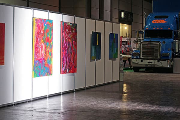 Farbenfrohe Gemälde an Stellwänden neben einem LKW in der Messehalle