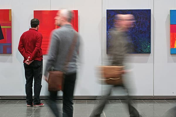 Besucher gehen an den ausgestellten Gemälden vorbei